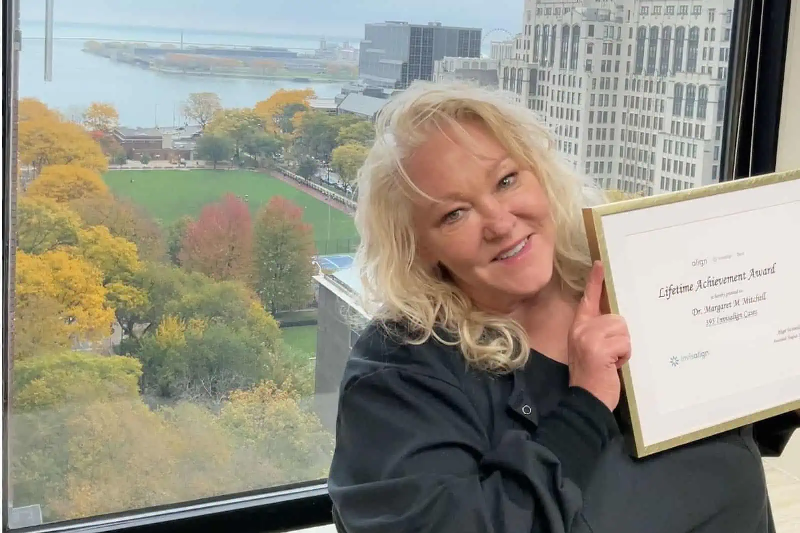 Dr. Margaret Mitchell proudly displaying her award for being the her Lifetime Achievement Award in front of a window showing the Chicago skyline.