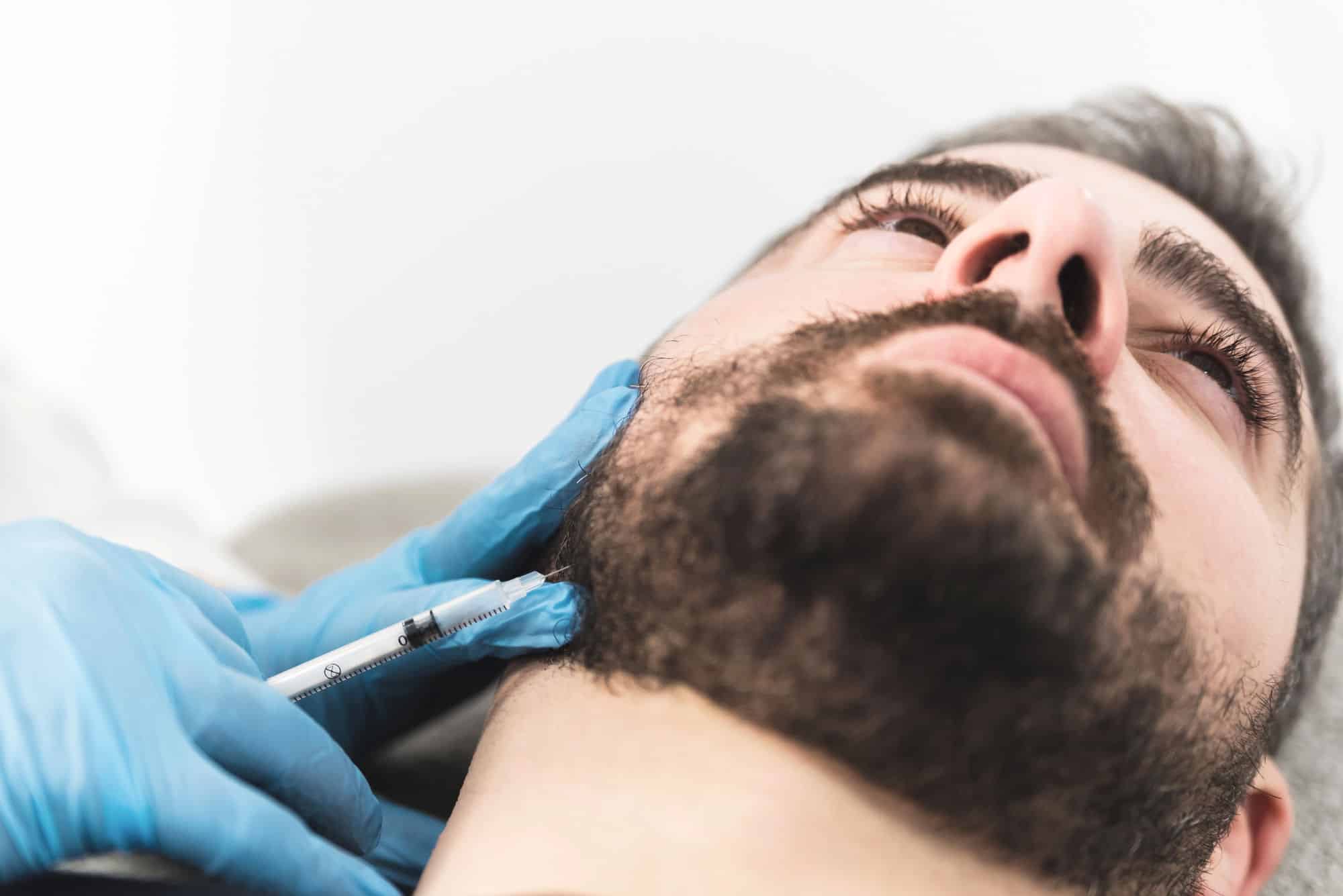 A white man with a short beard receives Botox to treat his TMJ pain through an injection.