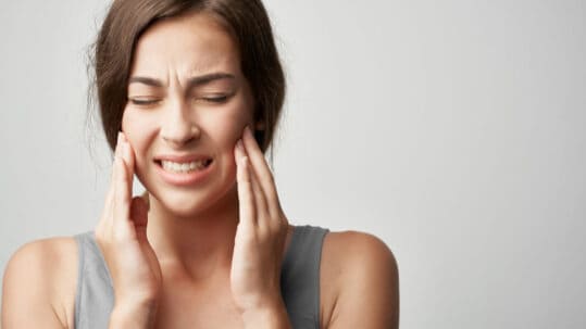 A young woman holds her jaw because of TMJ pain.