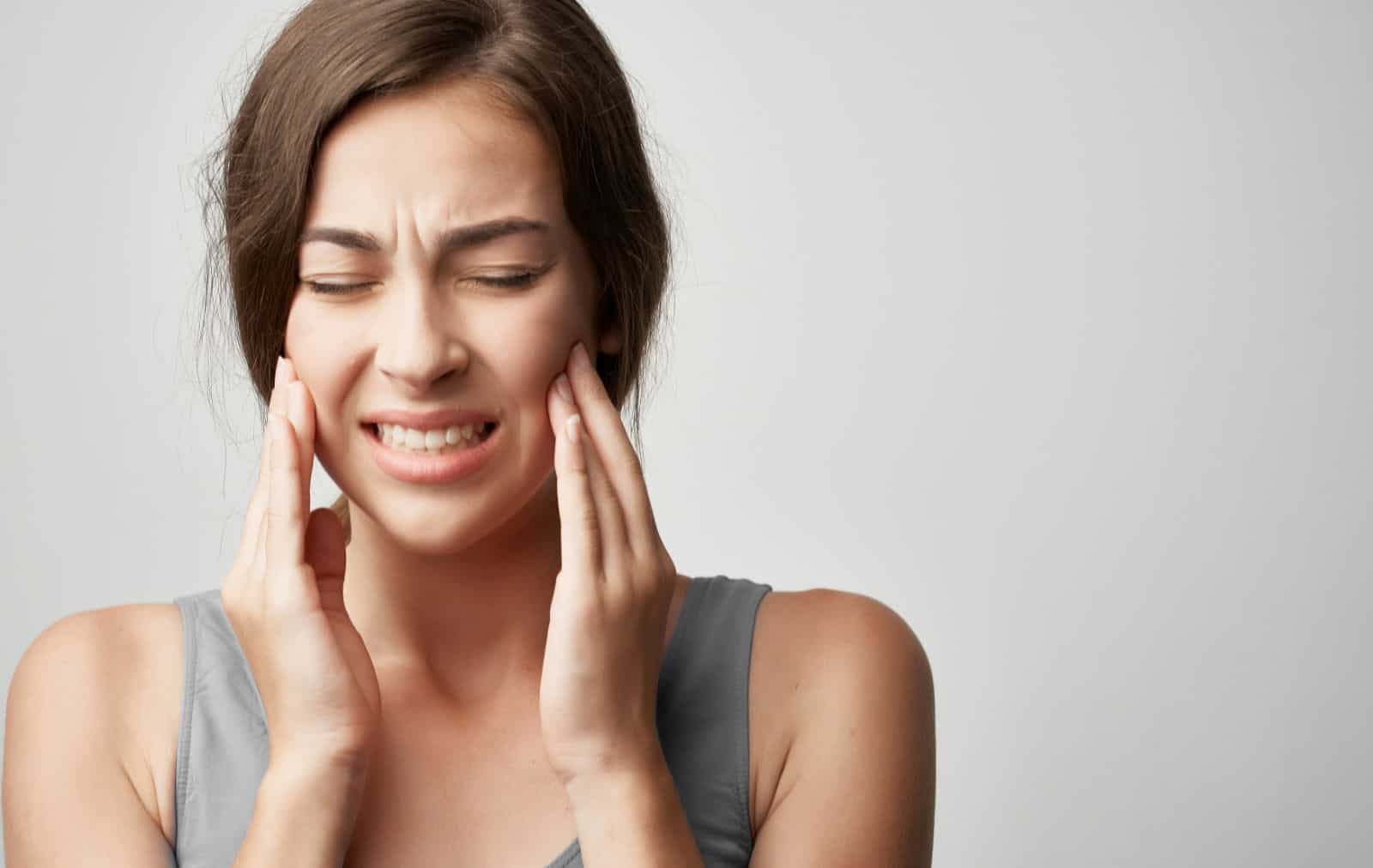 A young woman holds her jaw because of TMJ pain.