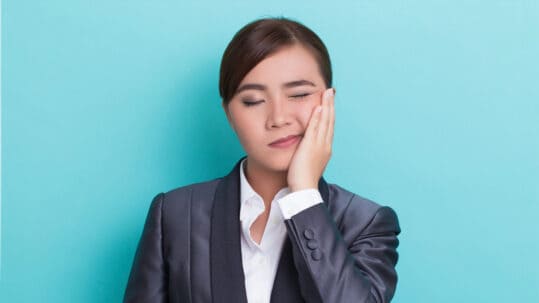 A woman suffering from TMJ holds her jaw in pain.