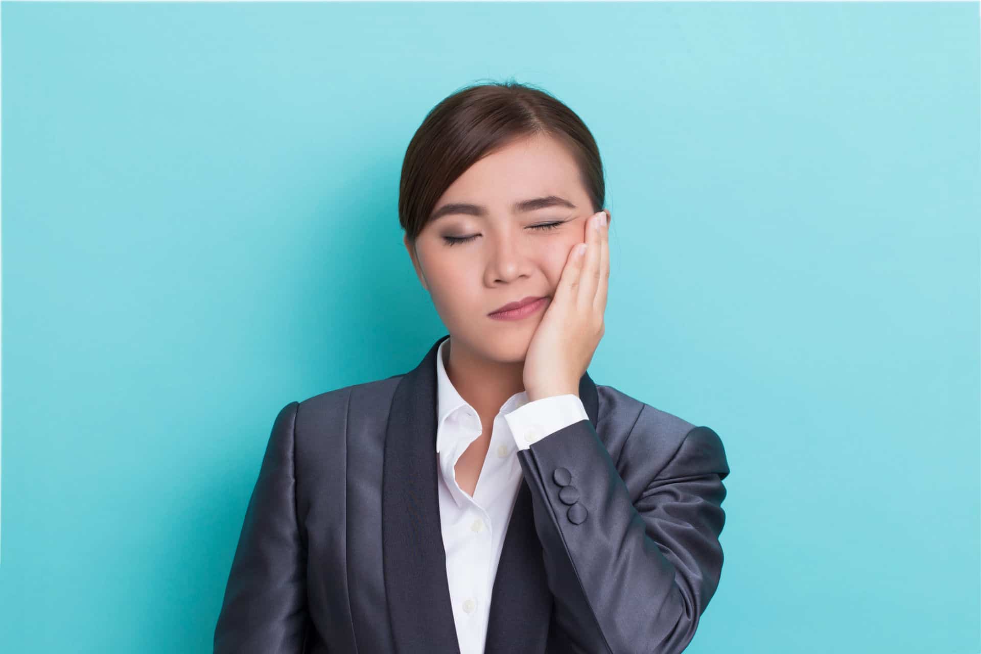 A woman suffering from TMJ holds her jaw in pain.